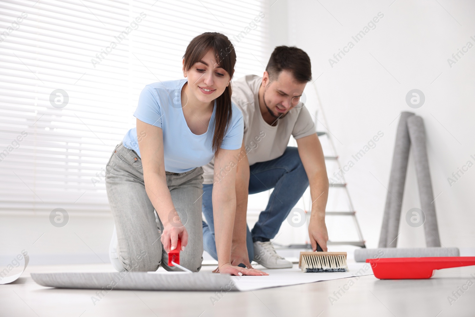 Photo of Couple applying glue onto wallpaper sheet in room