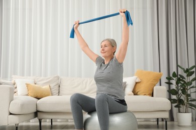 Senior woman doing exercise with elastic resistance band on fitness ball at home