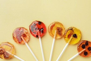 Sweet colorful lollipops with berries on beige background, flat lay