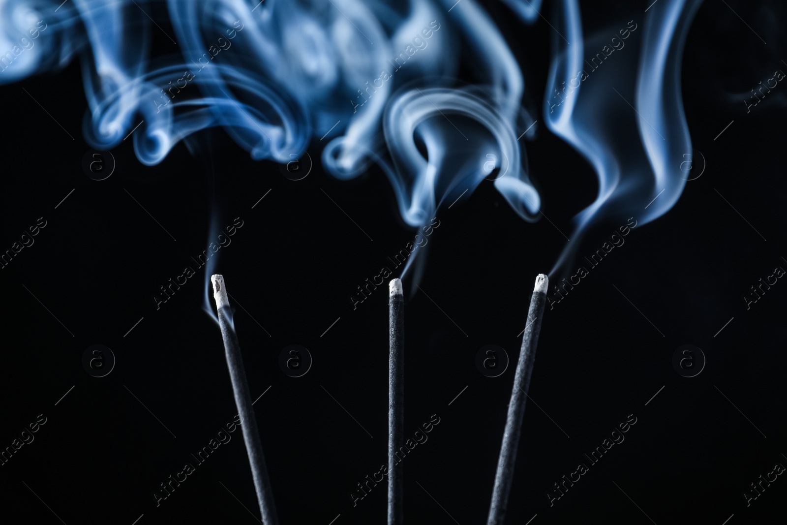 Photo of Incense sticks smoldering on black background, closeup