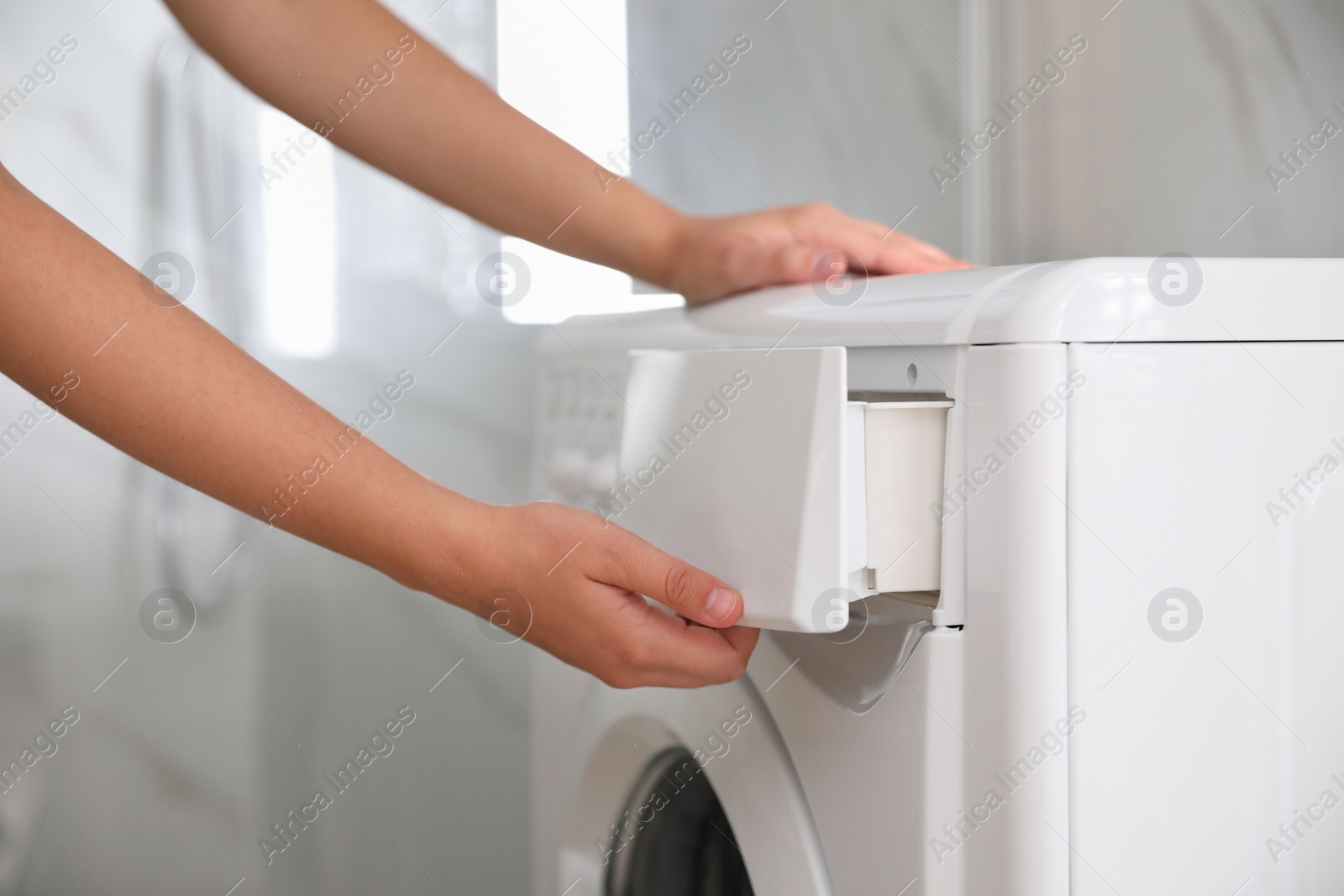 Photo of Woman opening detergent drawer of modern washing machine in bathroom, closeup