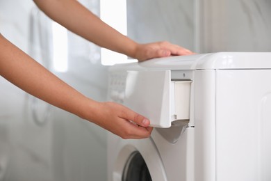 Woman opening detergent drawer of modern washing machine in bathroom, closeup