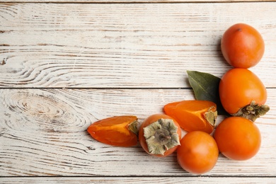 Photo of Delicious fresh persimmons on white wooden table, flat lay. Space for text