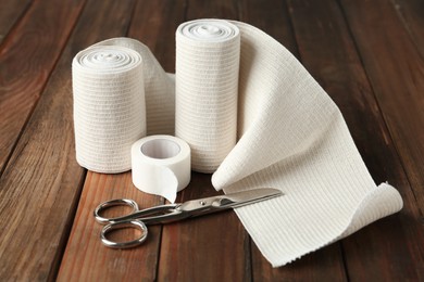 Photo of Medical bandage rolls, sticking plaster and scissors on wooden background