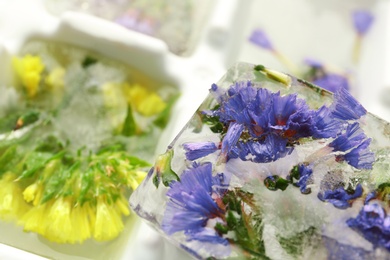 Ice cube with flowers on blurred background, closeup