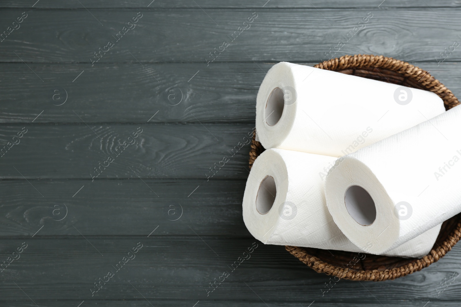 Photo of Rolls of paper towels in wicker basket on grey wooden table, top view. Space for text