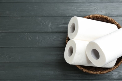 Rolls of paper towels in wicker basket on grey wooden table, top view. Space for text