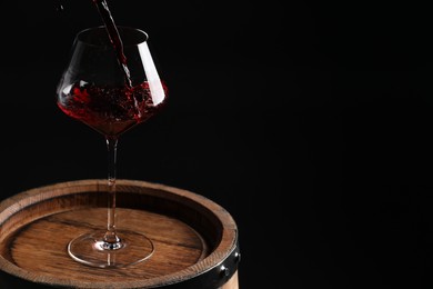 Photo of Pouring red wine into glass on wooden barrel against black background. Space for text