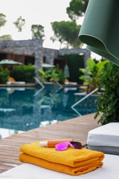 Photo of Beach towels, sunglasses and sunscreen on sun lounger near outdoor swimming pool, space for text. Luxury resort