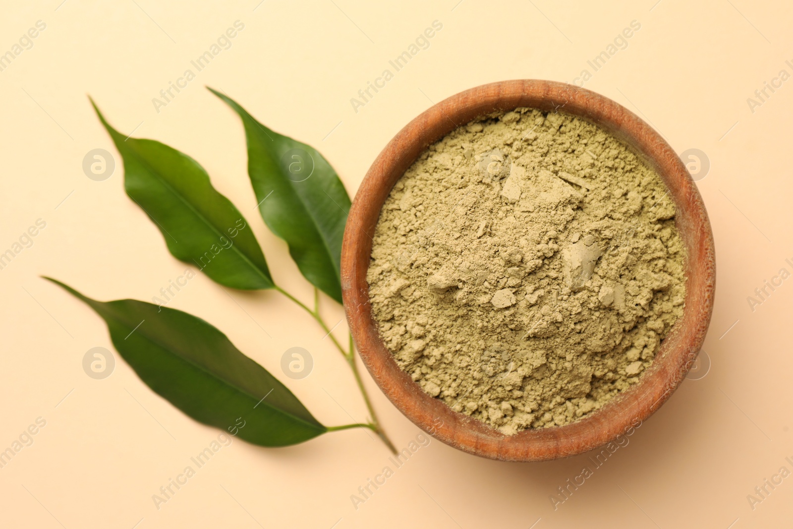 Photo of Henna powder and green leaves on beige background, flat lay. Natural hair coloring