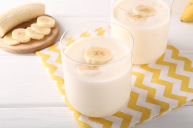 Photo of Tasty yogurt and banana in glasses on white wooden table, closeup