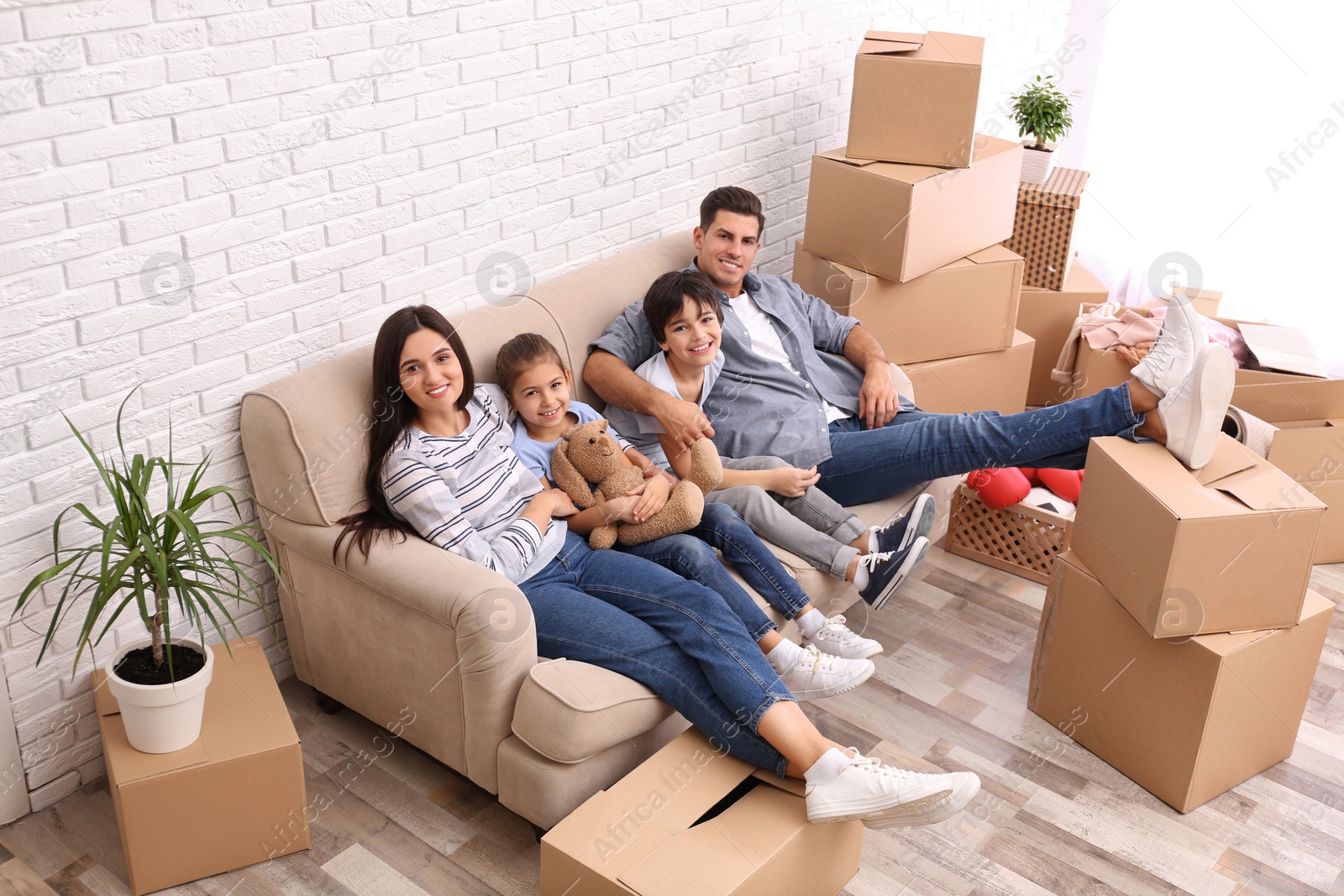 Photo of Happy family resting in room with cardboard boxes on moving day