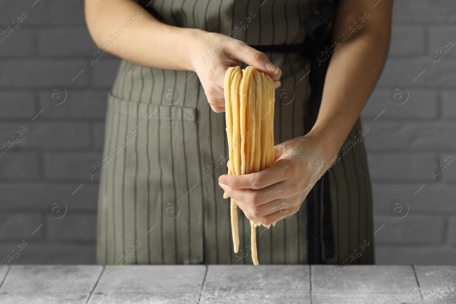 Photo of Woman with homemade pasta at light tiled table, closeup