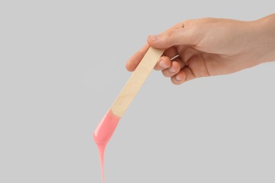 Photo of Woman holding spatula with hot depilatory wax on light  background, closeup