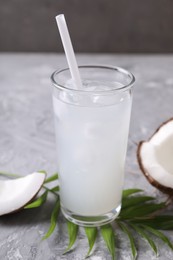 Photo of Glass of coconut water with ice cubes, palm leaf and nut on grey table