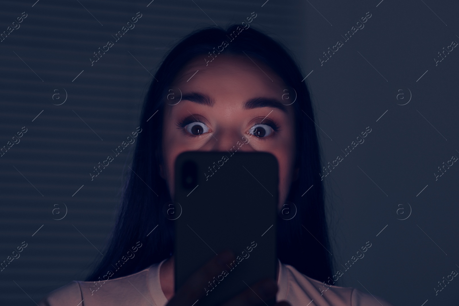 Photo of Woman using modern smartphone in dark room. Internet addiction