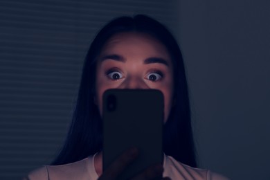 Photo of Woman using modern smartphone in dark room. Internet addiction