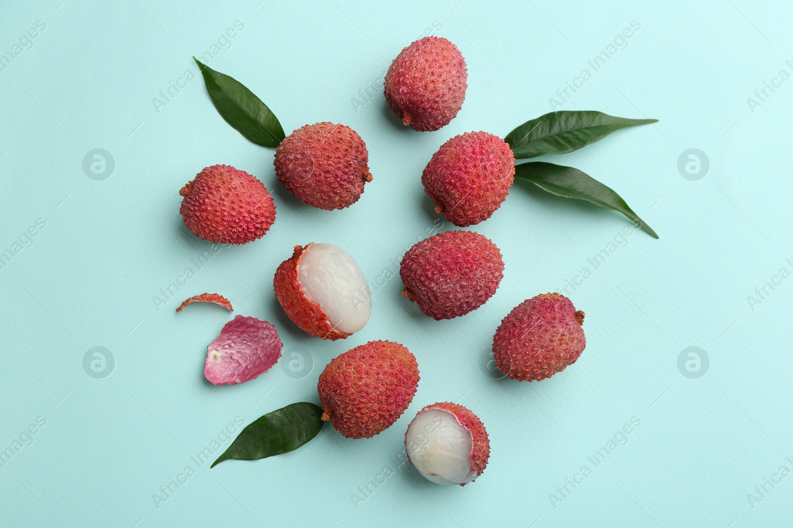 Photo of Fresh ripe lychees with leaves on turquoise background, flat lay