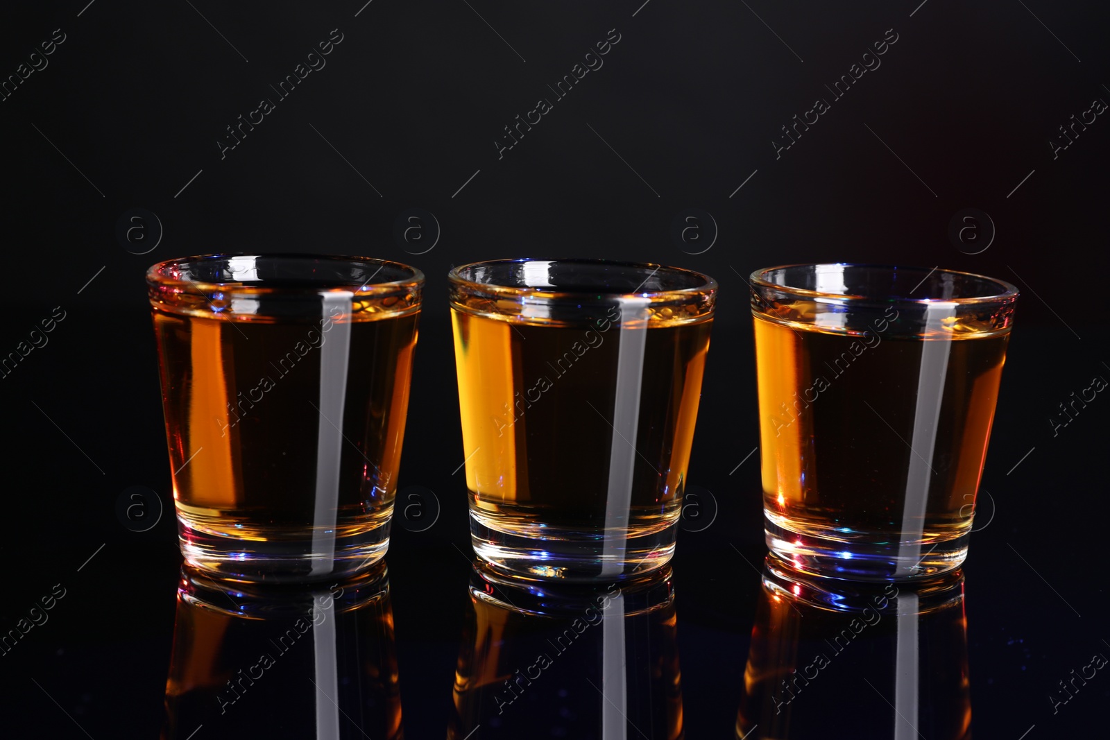 Photo of Alcohol drink in shot glasses on mirror surface, closeup