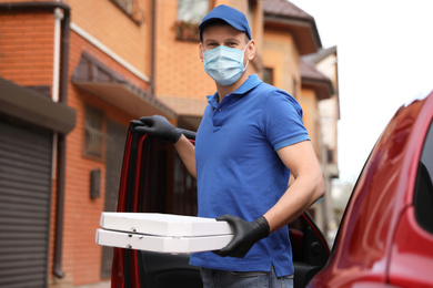 Courier in protective mask and gloves with pizza boxes near car outdoors. Food delivery service during coronavirus quarantine