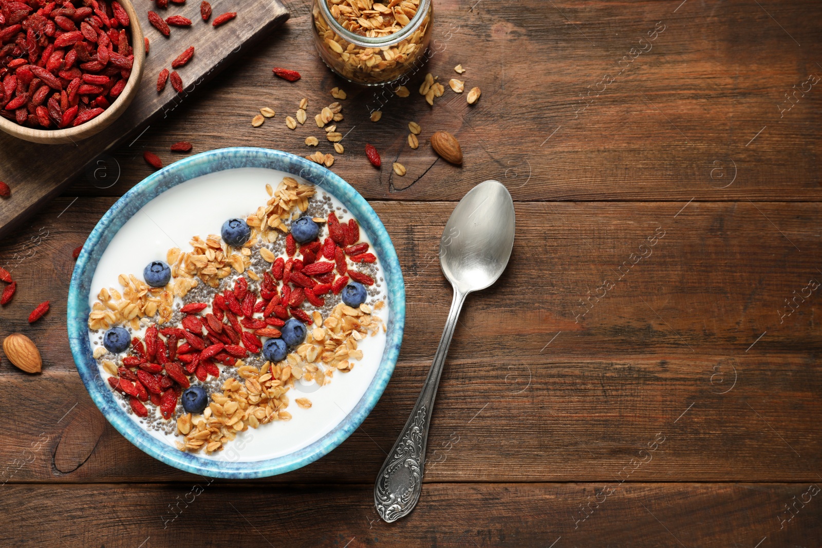 Photo of Flat lay composition of smoothie bowl with goji berries on wooden table. Space for text