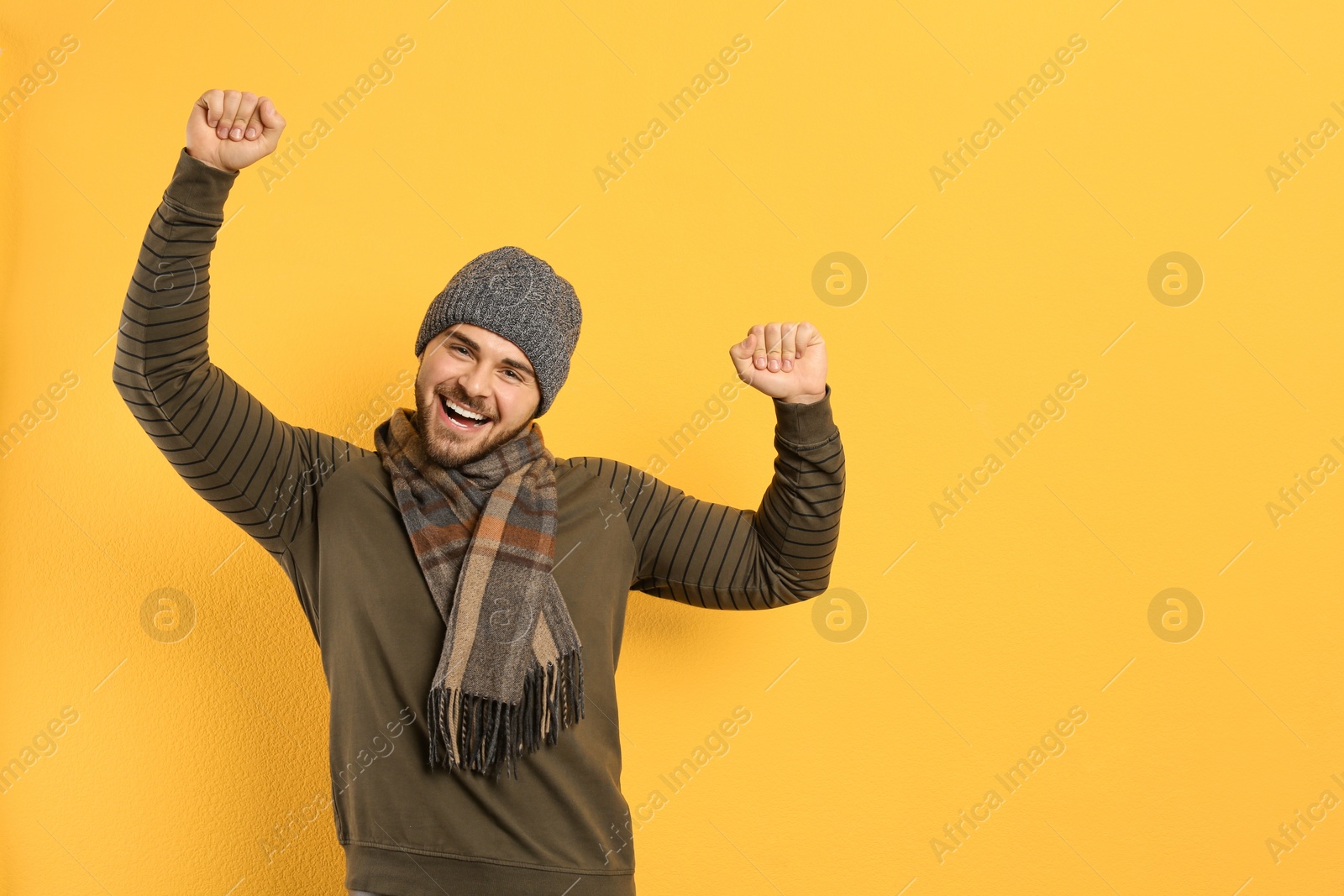 Photo of Happy young man in warm clothes on yellow background, space for text. Winter vacation