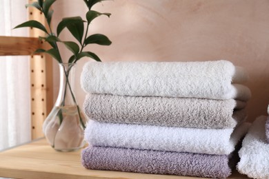 Stacked soft towels and green leaves on wooden shelf indoors