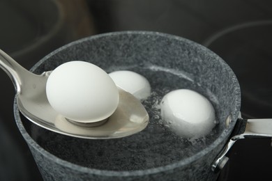 Photo of Spoon with boiled egg above saucepan on electric stove, closeup