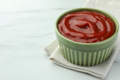 Photo of Bowl of tasty ketchup on white marble table, closeup. Space for text