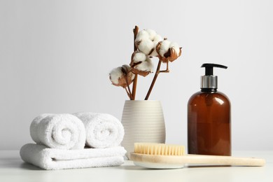 Photo of Different bath accessories and cotton flowers in vase on light table against white wall