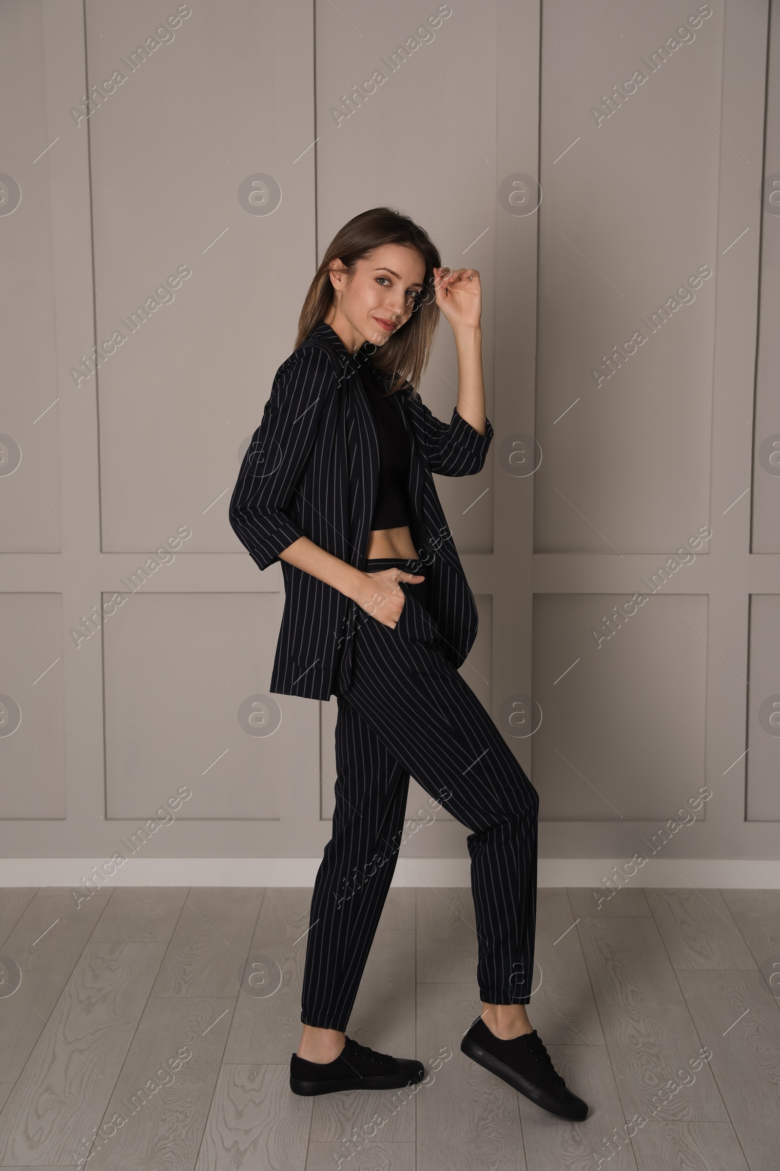 Photo of Full length portrait of beautiful young woman in fashionable suit near light grey wall indoors. Business attire