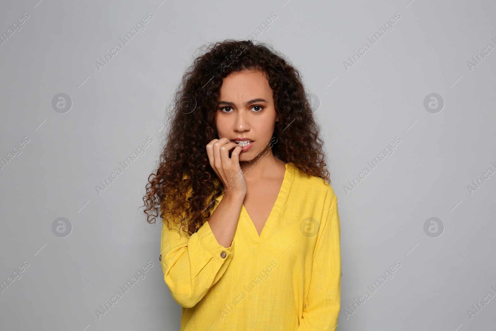 Photo of African-American woman biting her nails on grey background