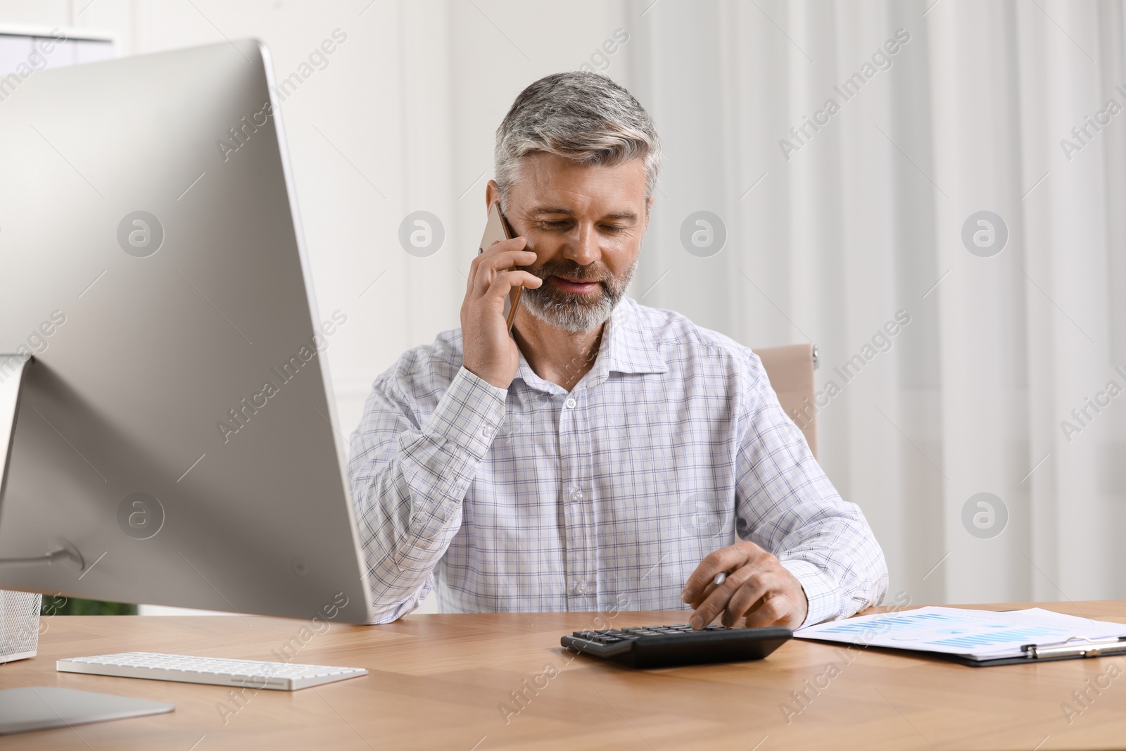 Photo of Professional accountant talking on phone and working at wooden desk in office