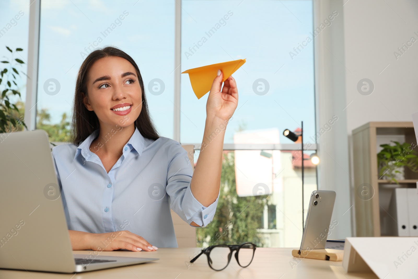 Photo of Beautiful young woman playing with paper plane at desk in office