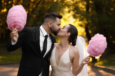 Photo of Newlywed couple with cotton candies kissing in park