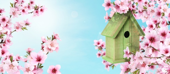Image of Beautiful wooden bird house hanging on blossoming tree outdoors, banner design. Springtime