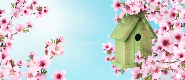 Beautiful wooden bird house hanging on blossoming tree outdoors, banner design. Springtime