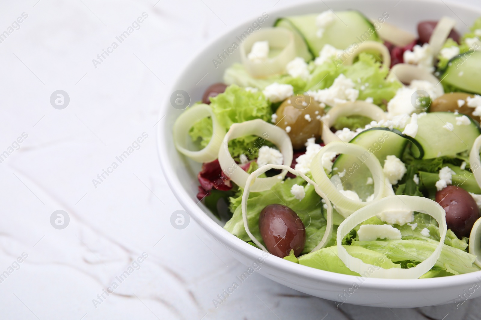 Photo of Bowl of tasty salad with leek, olives and cheese on white textured table, closeup. Space for text