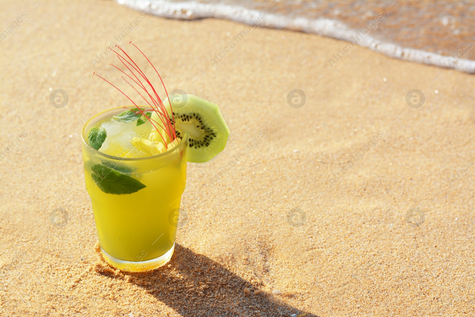Glass of refreshing drink with kiwi and mint on sand near sea. Space for text Photo of Glass of refreshing drink with kiwi and mint on sand near sea. Space for text