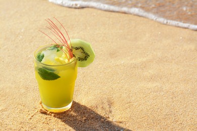 Photo of Glass of refreshing drink with kiwi and mint on sand near sea. Space for text