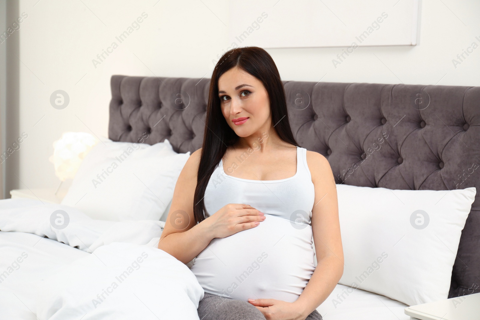 Photo of Beautiful pregnant woman sitting on bed at home