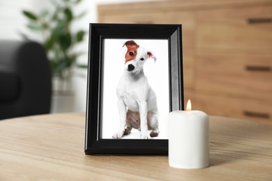 Frame with picture of dog and burning candle on wooden table indoors. Pet funeral