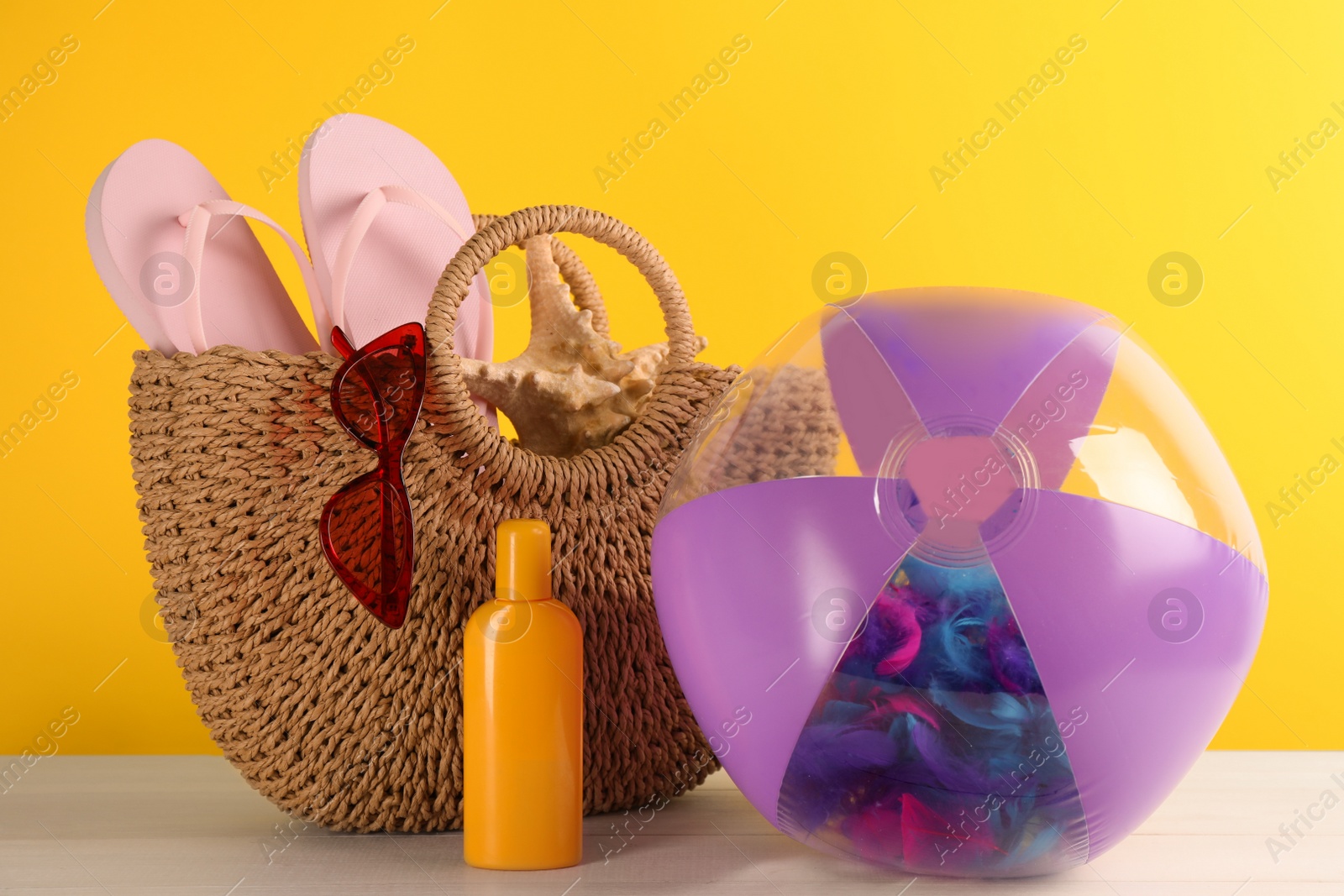 Photo of Bright inflatable ball and bag with beach accessories on white wooden table against yellow background