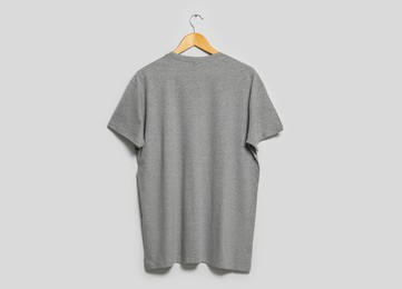 Photo of Hanger with grey t-shirt on light wall. Mockup for design