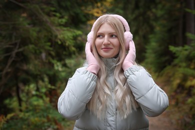 Photo of Young beautiful woman wearing warm earmuffs in forest