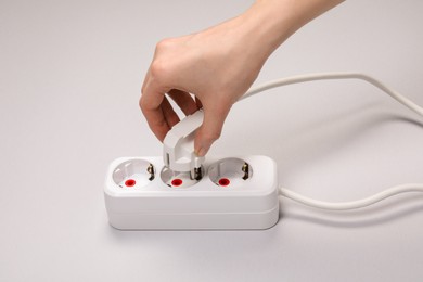 Woman putting plug into power strip on white background, closeup