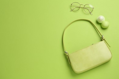 Photo of Stylish baguette bag, glasses and lip balm on light green background, flat lay, Space for text