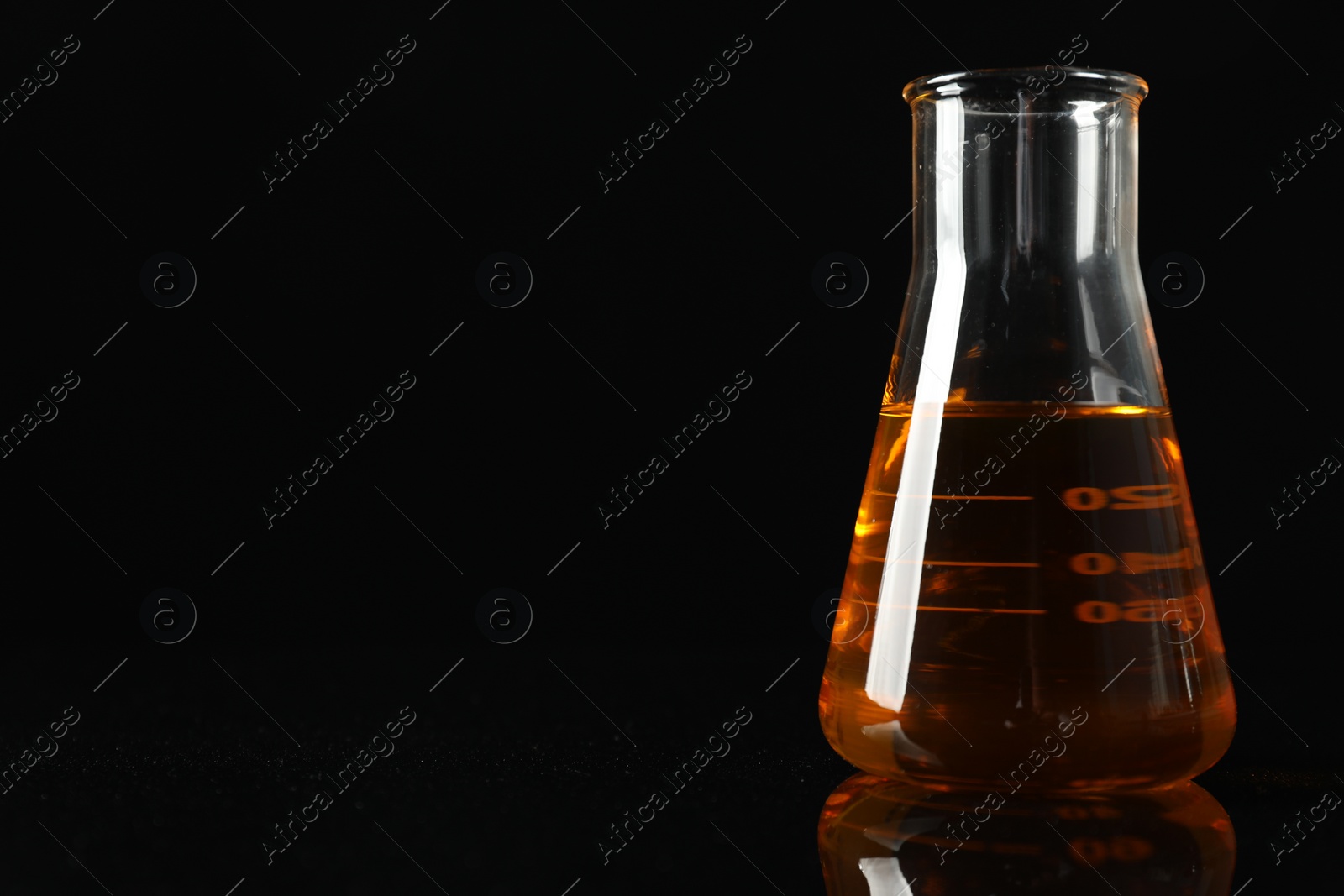 Photo of Glass flask with yellow oil on black background, closeup. Space for text