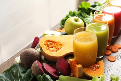 Glasses with different juices and fresh ingredients on wooden table. Space for text