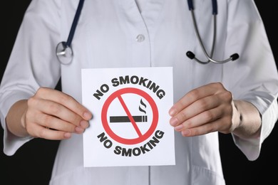 Photo of Doctor holding card with no smoking sign on black background, closeup